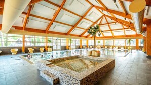 Ein großes Hallenbad mit bepflasterter Liegefläche, Holzbalken und sonnendurchfluteten Fenstern.