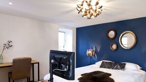 Ein Schlafzimmer mit Bett, Schreibtisch, Stuhl, Fernseher und einem dekorativen Spiegel.