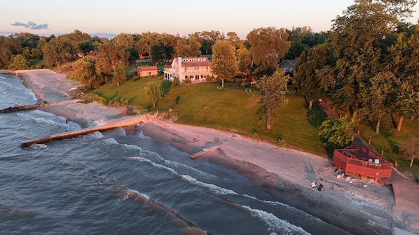 A coastal property with a large house, a beach, and a wooden deck.
