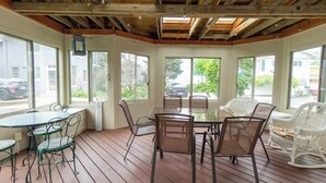 A covered patio with a table and chairs, large windows, and a wooden ceiling.
