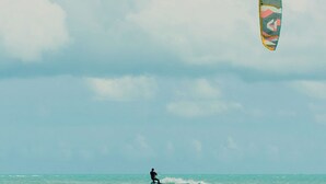 Una persona practicando windsurf en un mar tranquilo con una cometa colorida.