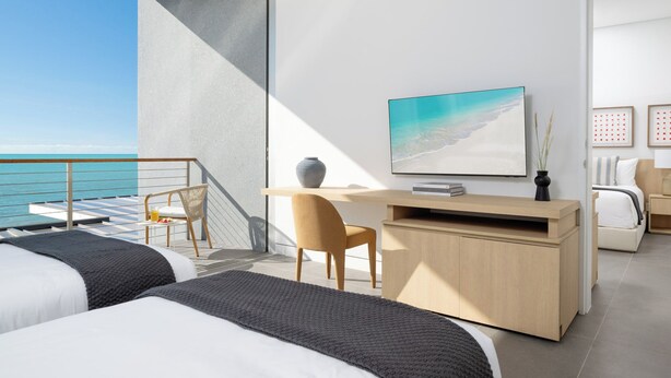 Un dormitorio moderno con balcón, escritorio, televisor y cama.