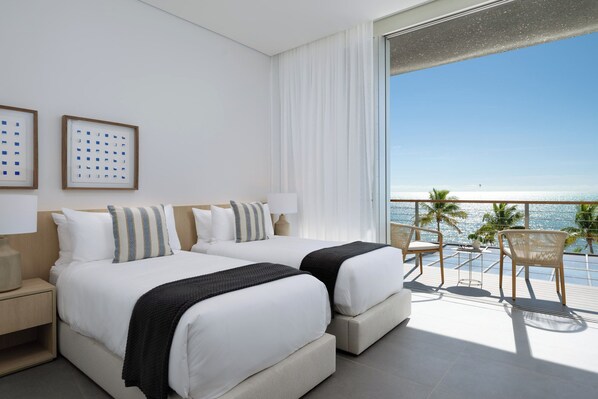 Habitación de hotel con dos camas, un balcón con sillas y vista al mar.