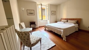 Quarto com cama, cadeira, mesa pequena e janela.