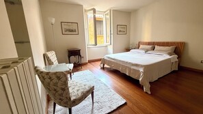Ein Schlafzimmer mit einem Bett, einem Sessel, einem kleinen Tisch und einem Fenster.