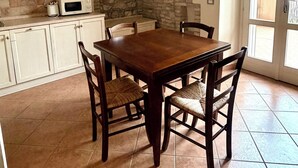 Uma área de refeições com mesa e cadeiras de madeira, micro-ondas na bancada e parede de pedra.