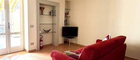 A living room with a red sofa, a flat-screen TV, a bookshelf, and a door leading outside.