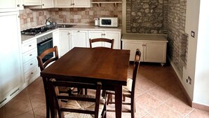 Cozinha com armários brancos, arco de pedra, piso ladrilhado e mesa de jantar com cadeiras.