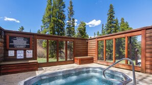 A hot tub with a wooden deck, a sign with hot tub rules, and a view of trees. - Ski-In Mountain Condo | Perfect for Families & Groups (Breckenridge)