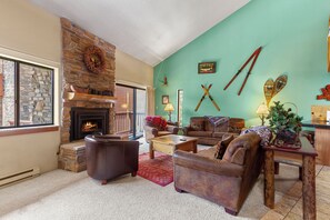 A cozy living room with a stone fireplace, leather sofas, and skis mounted on the wall. - Ski-In Mountain Condo | Perfect for Families & Groups (Breckenridge)