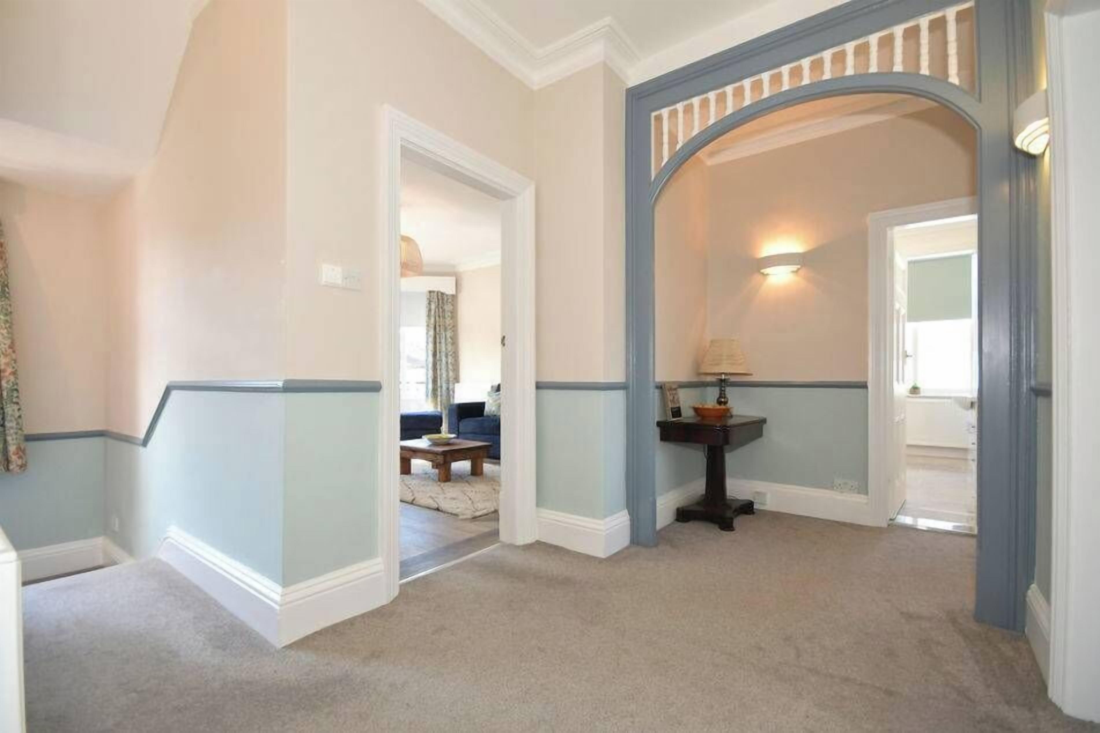 A hallway with a blue and white wainscoting, a black console table, and a light fixture.