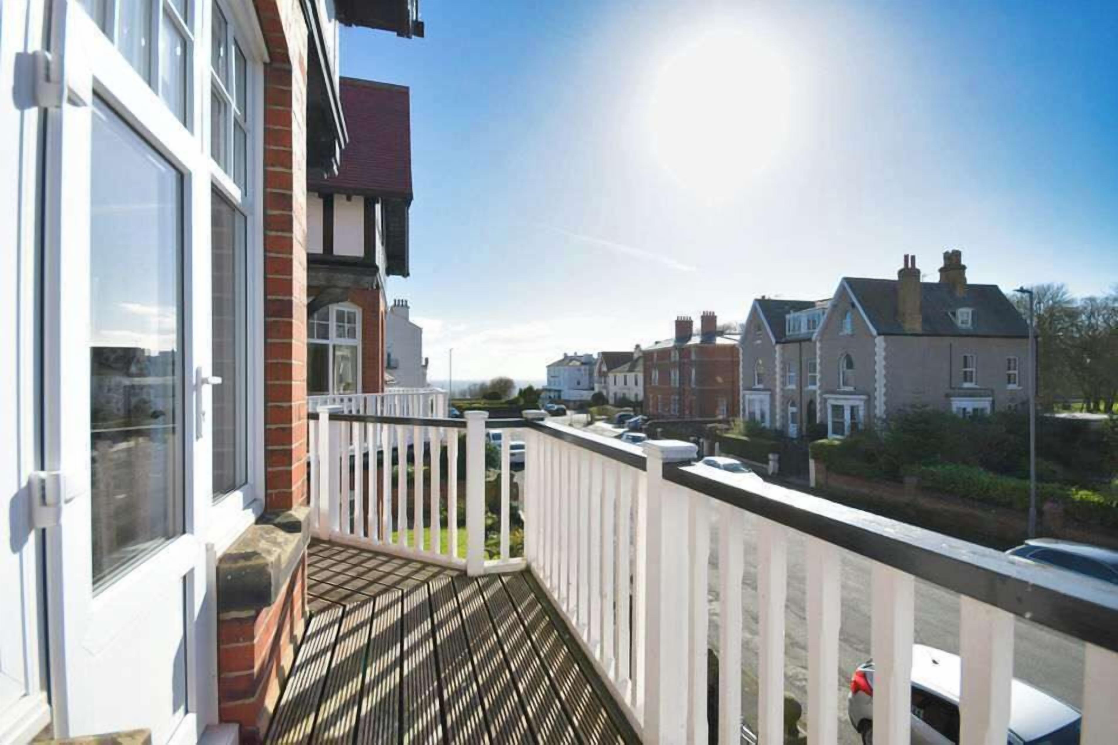 A residential balcony with a view of neighboring houses, a clear sky, and a sunny day.