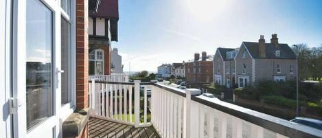 A residential balcony with a view of neighboring houses, a clear sky, and a sunny day.