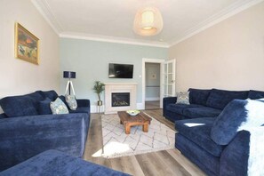 Ein Wohnzimmer mit zwei blauen Sofas, einem Kamin, einem Fernseher und einer Hängeleuchte.