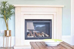 A fireplace with logs, a potted plant, and a wooden table with a bowl. - St Oswalds - Four-Bedroom Edwardian Apartment (North Yorkshire)