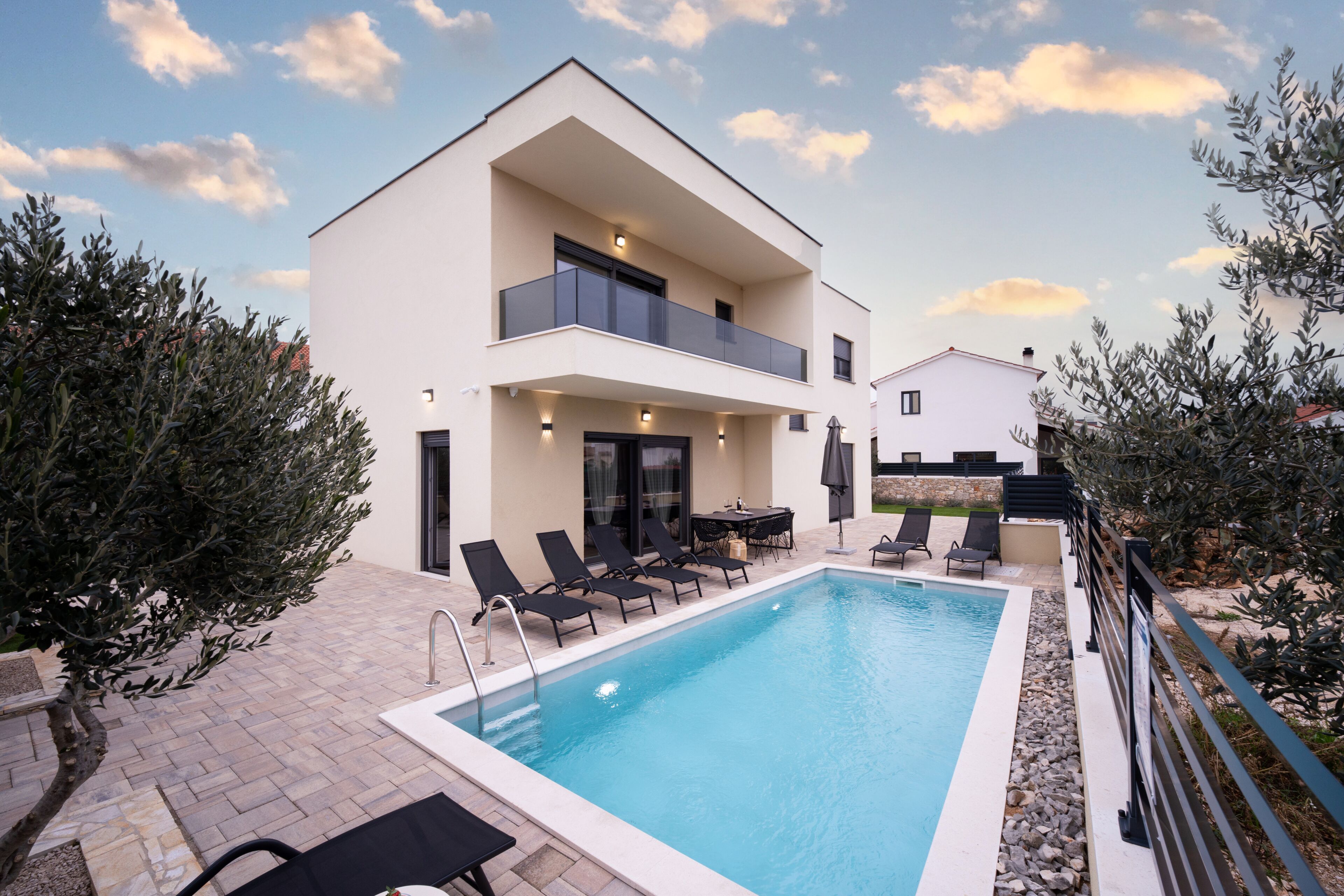A modern two-story building with a swimming pool, outdoor seating, and a balcony.