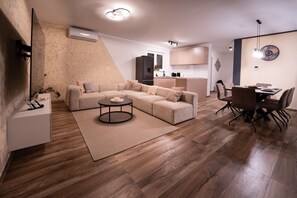 Ein modernes Wohnzimmer mit Ecksofa, rundem Couchtisch und Essbereich mit Tisch und Stühlen.