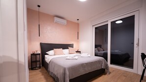 Un dormitorio con cama, mesitas de noche, aire acondicionado, una mesita redonda y una puerta corredera que da a otra habitación.