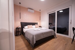 Ein Schlafzimmer mit Bett, Nachttischen, einer Klimaanlage, einem runden Beistelltisch und einer Schiebetür zu einem weiteren Raum.