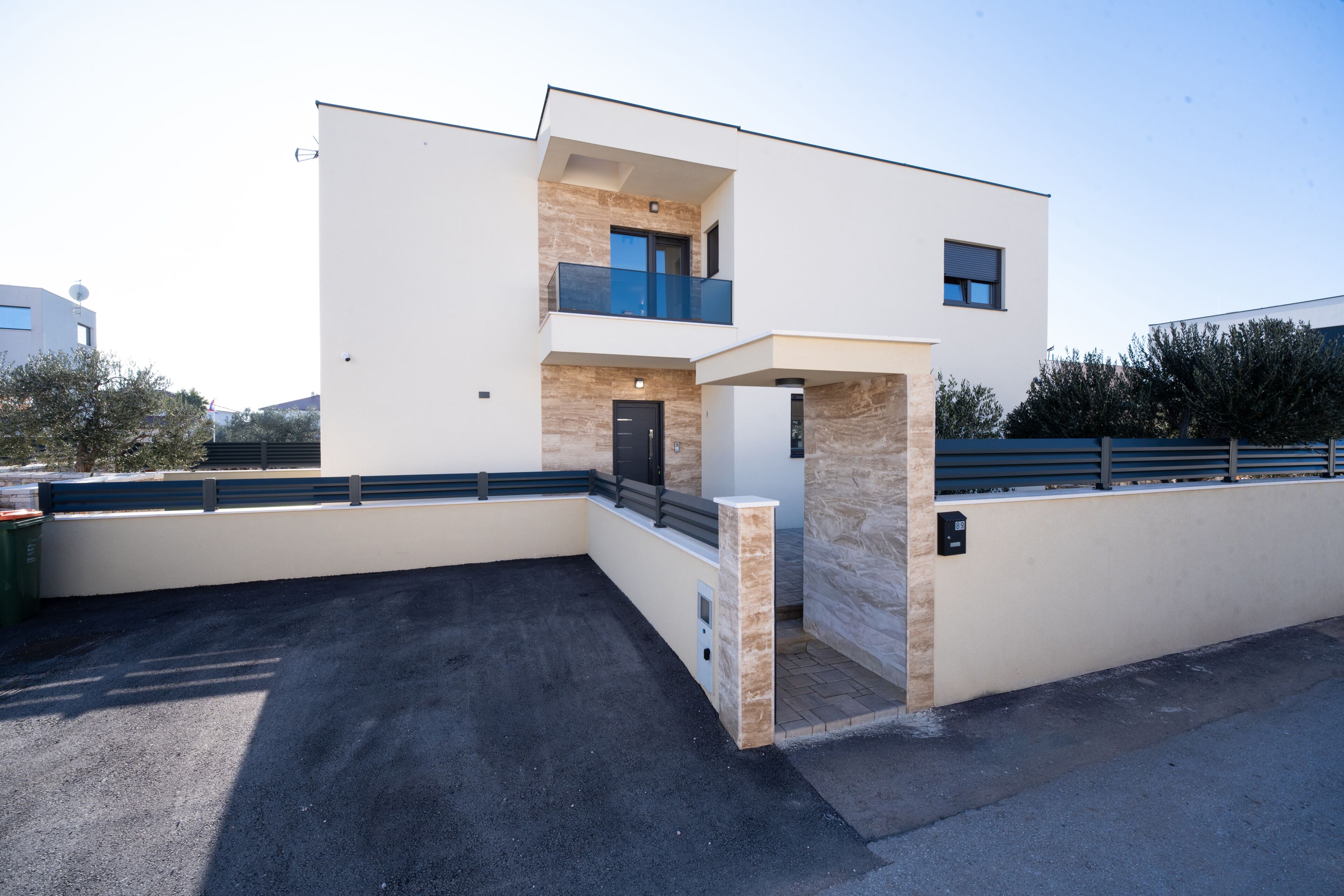 A modern two-story building with a flat roof, a balcony, and a stone facade.