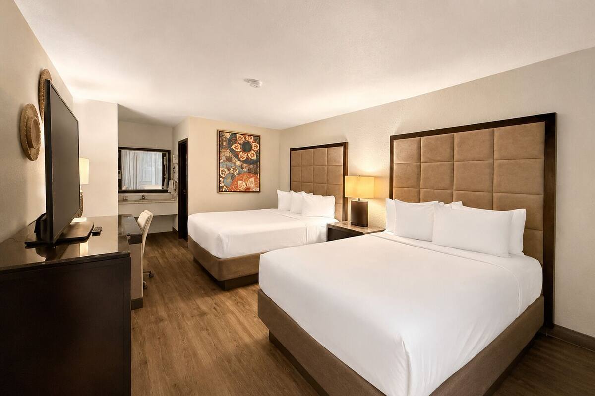 Ein Hotelzimmer mit zwei Betten, einem Schreibtisch, einem Fernseher und einem Bild an der Wand.