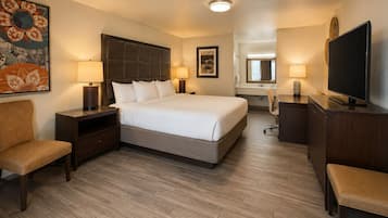 A hotel room with a bed, two bedside tables with lamps, a chair, a desk with a television, and a large mirror.