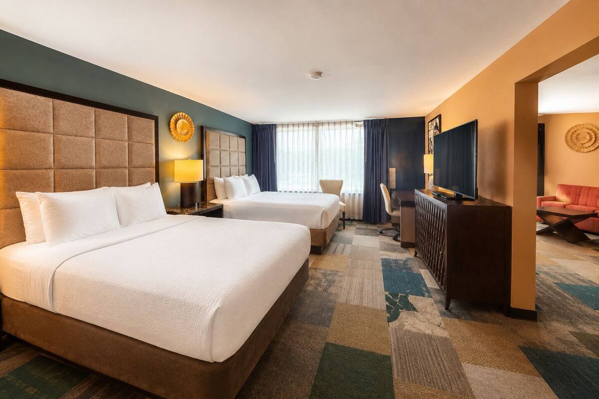Ein Hotelzimmer mit zwei Betten, einem Schreibtisch, einem Fernseher und einer Sitzecke.