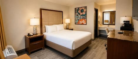 A hotel room with a bed, bedside tables, a chair, a desk, a mirror, and a wall art piece.