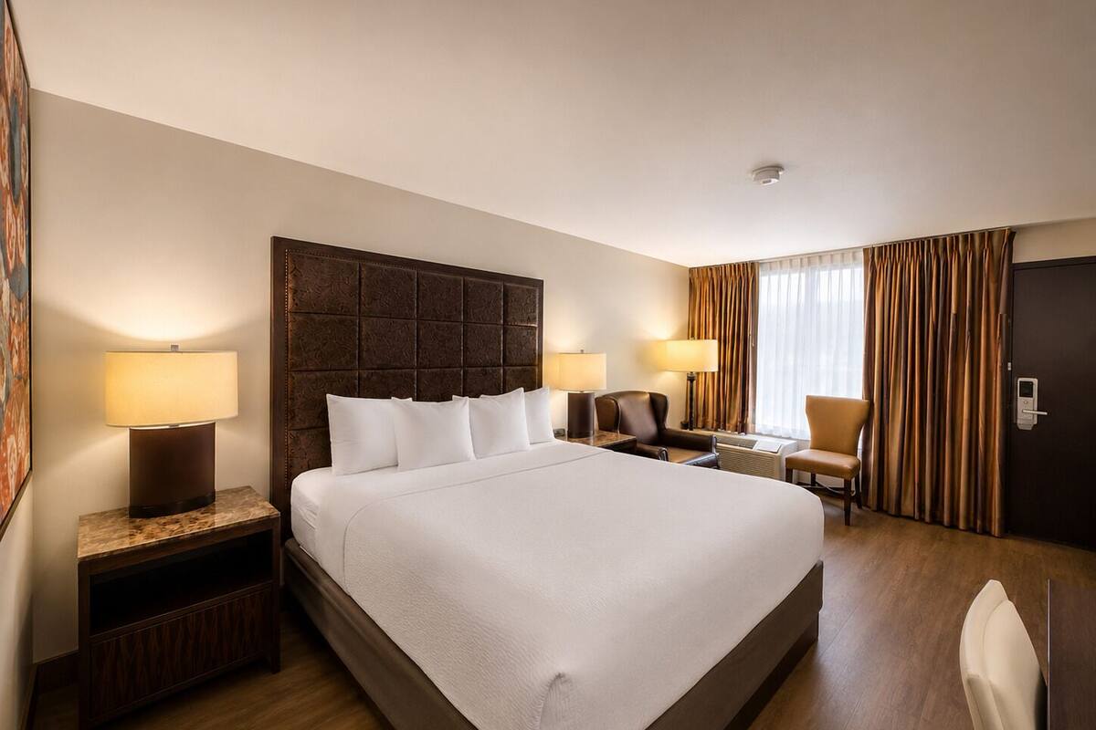 Ein Hotelzimmer mit einem großen Bett, zwei Nachttischen mit Lampen, einem Sessel, einem Schreibtisch und einer Tür.