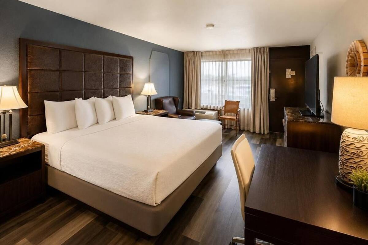 Ein Hotelzimmer mit einem großen Bett, einem Schreibtisch, einem Stuhl, einem Fernseher und einem Fenster mit Vorhängen.