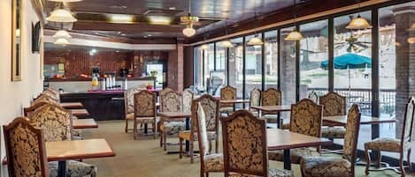 Un restaurante con mesas y sillas de madera, ventanas amplias y una barra.