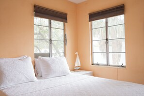Ein Schlafzimmer mit einem Bett, zwei Fenstern mit Jalousien, einem Nachttisch und einer Bootsdekoration.