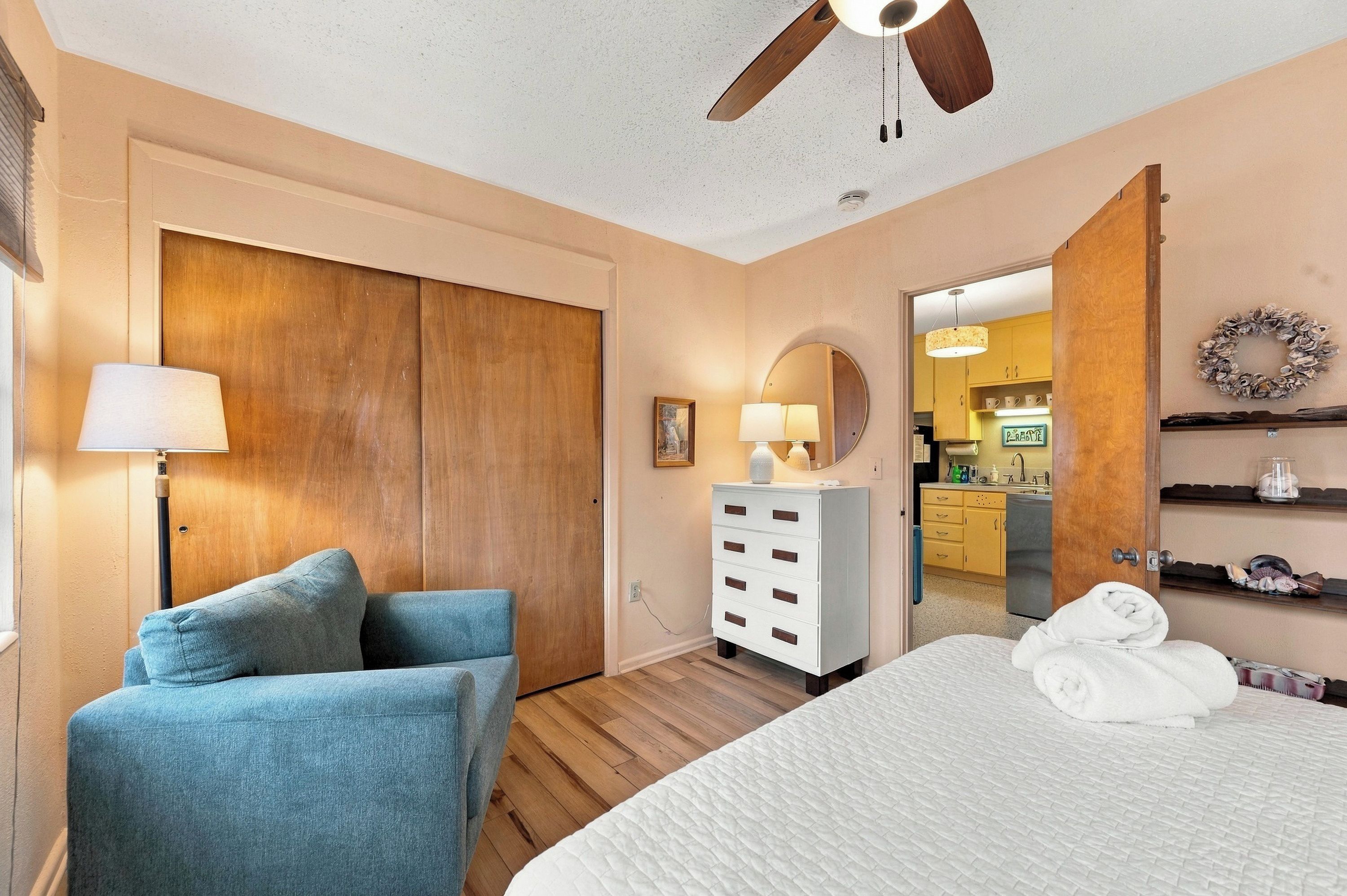 Une chambre à coucher avec un lit, une chaise, une commode et un ventilateur de plafond.