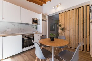 Eine moderne Küche mit weißen Schränken, einem eingebauten Ofen und einer Mikrowelle. Es steht ein runder Holztisch mit Stühlen und einem Blumentopf da.