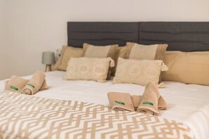 Ein ordentlich bezogenes Bett mit einer gemusterten Tagesdecke, mehreren Kissen und zusammengerollten Handtüchern in einem Hotelzimmer.