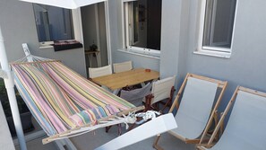 Eine Hängematte, ein Holztisch und zwei Staffeleien in einem Raum mit Fenstern und einer Tür.