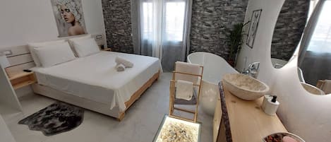 A modern bedroom with a bed, a bathtub, a vanity, and a small window.