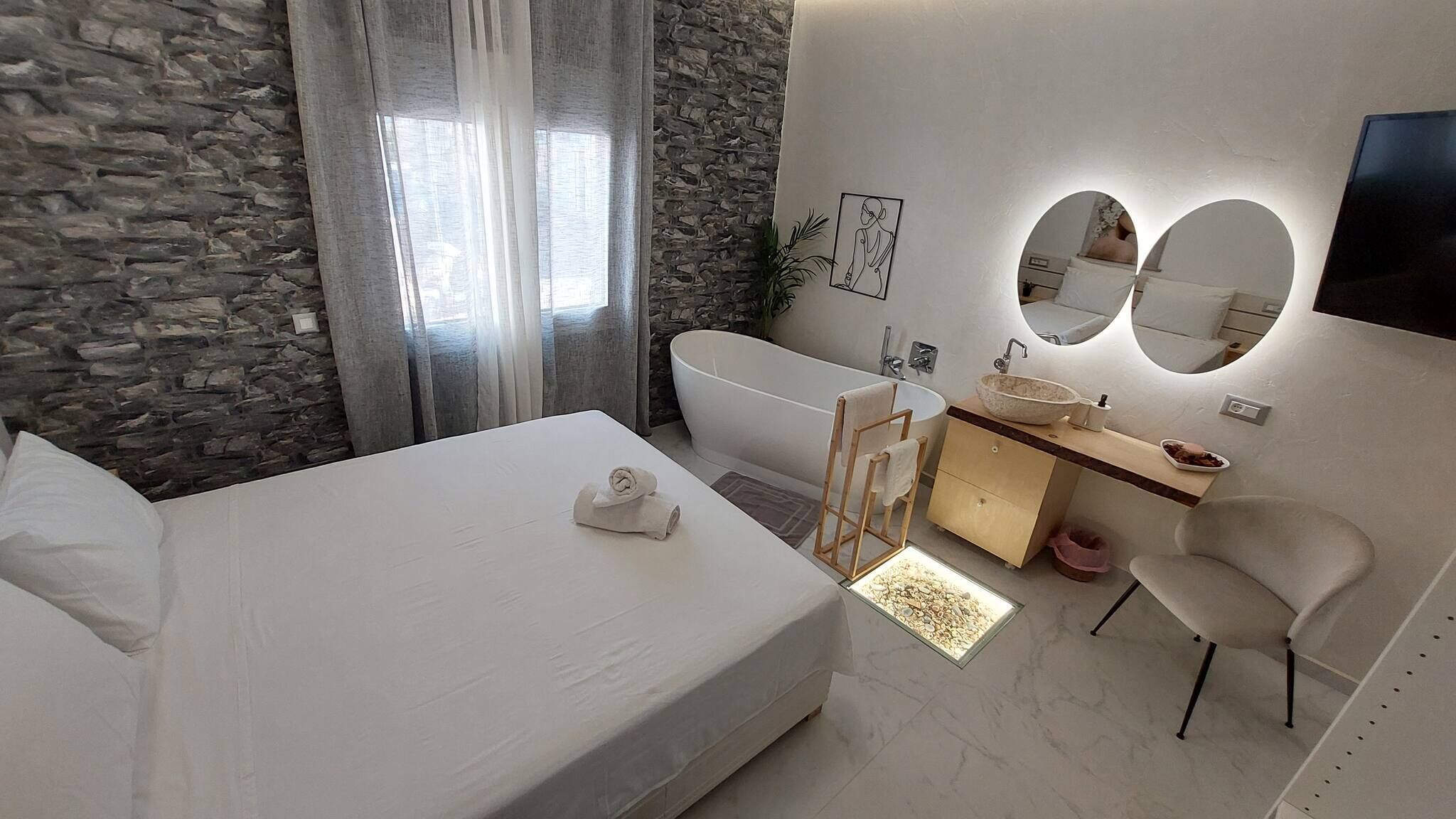 Een moderne slaapkamer met een groot bed, een badkuip, een wastafel met spiegel, en een stenen muur.