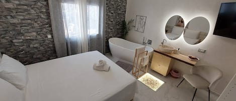 Un dormitorio moderno con una cama grande, una bañera, un tocador con espejo y una pared de piedra.