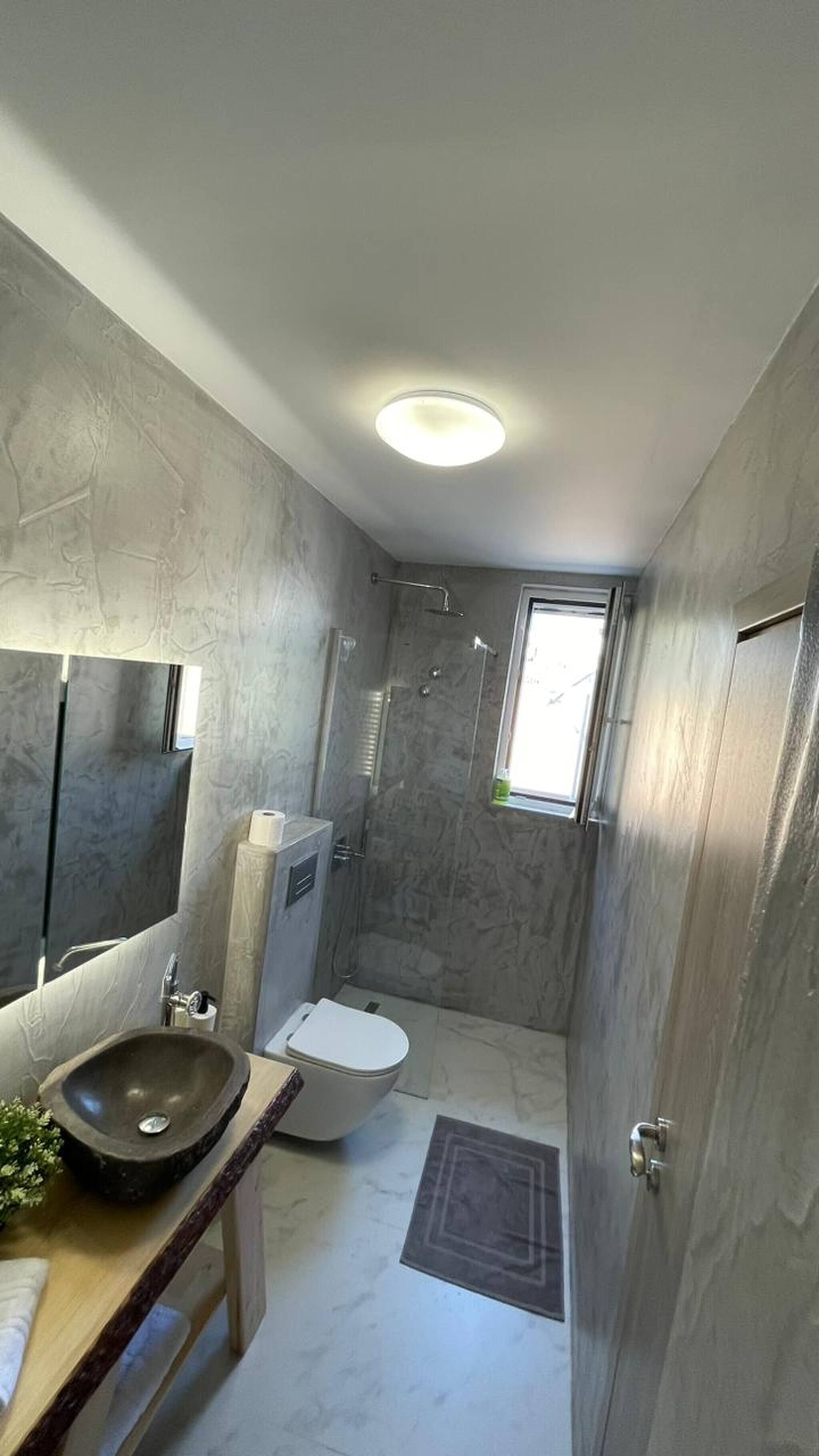 Et badeværelse med vask, toilet og brusebad samt et vindue.