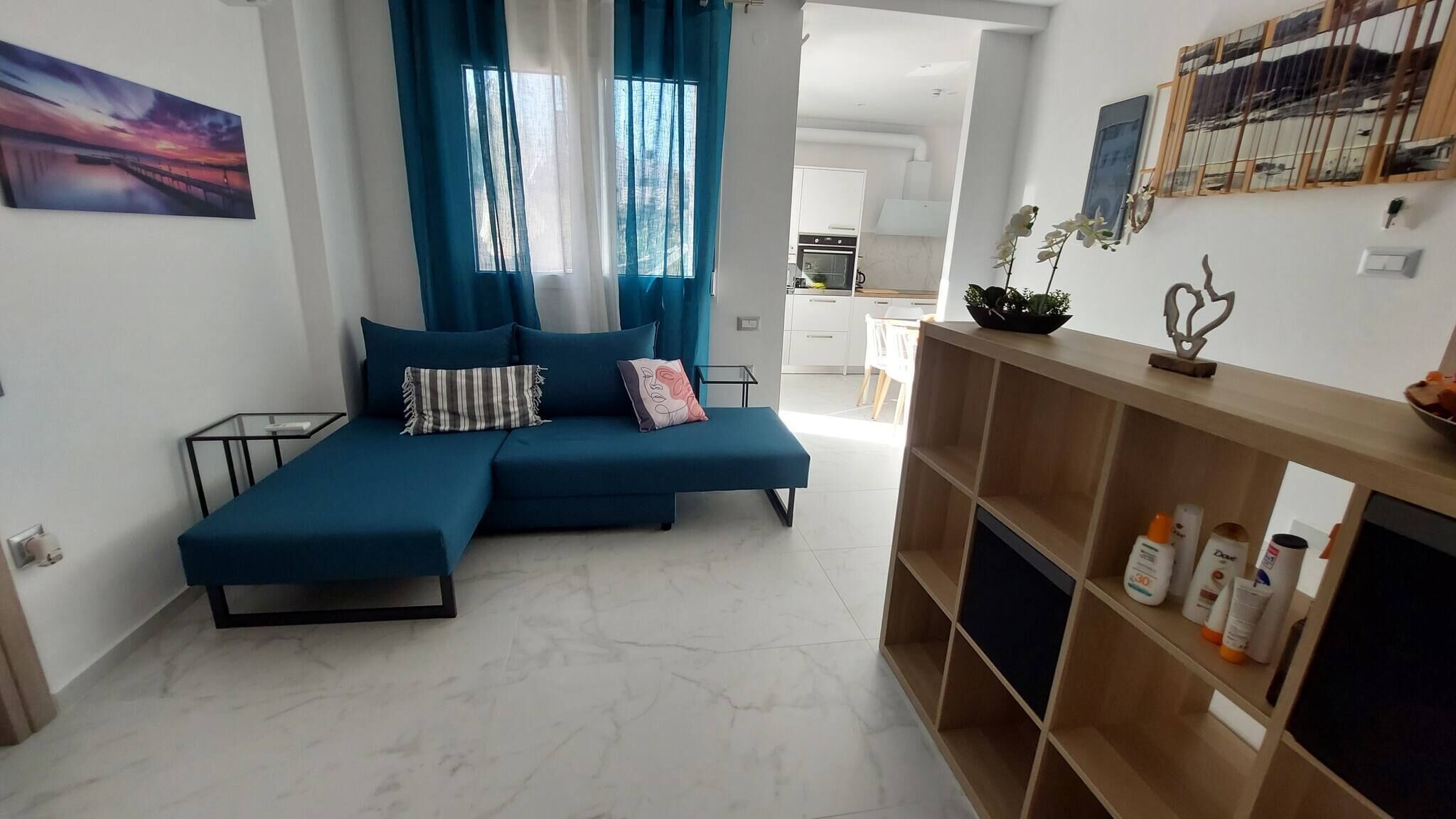 Un salon moderne avec un canapé d’angle, une table basse en verre et une console en bois sur laquelle sont posées des bouteilles.