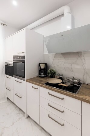 A modern kitchen with white cabinetry, a built-in oven, a stove, and a coffee maker. - My Hersonissos Home - Luxury Suite (Hersonissos)