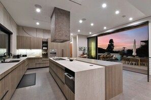 Une cuisine moderne dotée d’un grand îlot central, d’appareils électroménagers intégrés et offrant une vue sur le coucher de soleil.