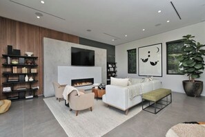A modern living room with a fireplace, a sofa, a coffee table, and a bookshelf. - Round Valley Residence - Sherman Oaks Hillside Retreat with Pool and Spa (Sherman Oaks, Los Angeles)