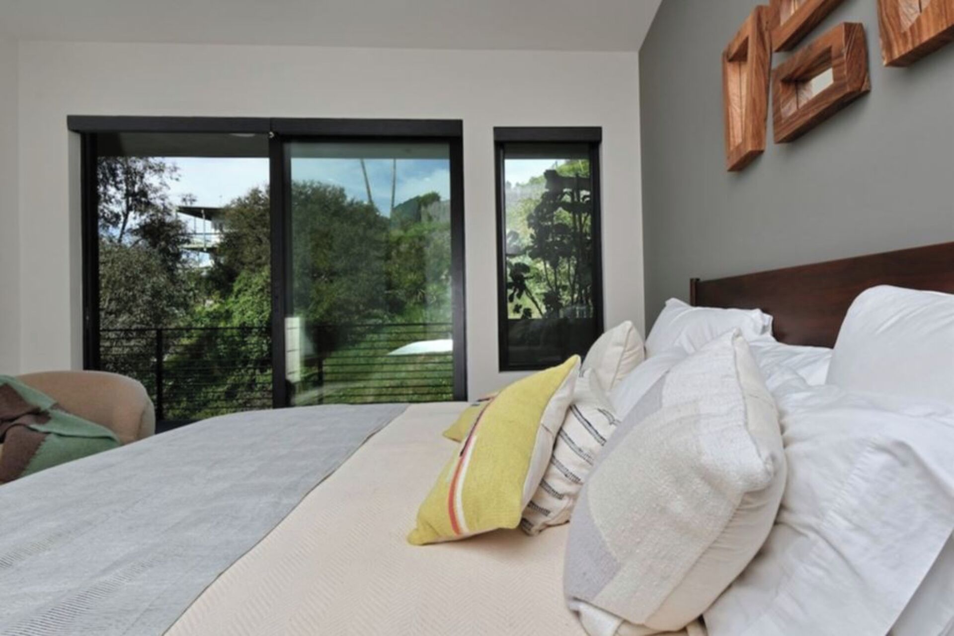 A bedroom with a bed, pillows, a view through a sliding door to an outdoor area, and a wooden headboard.