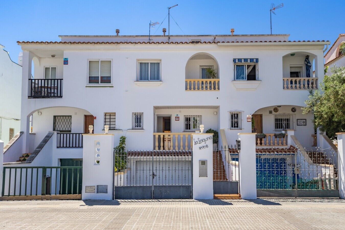A multi-story residential building with a white facade, balconies, and a gated entrance.