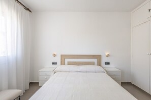 Une chambre à coucher au style minimaliste, avec un lit, deux tables de chevet, un banc et une armoire.