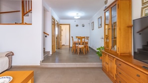 A hallway leading to a dining area with a wooden table and chairs, a TV on the right, and a staircase on the left. - Penthouse with Private Sun Deck, BBQ, and Beach (Cunit)