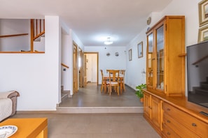 A hallway leading to a dining area with a wooden table and chairs, a TV on the right, and a staircase on the left. - Penthouse with Private Sun Deck, BBQ, and Beach (Cunit)