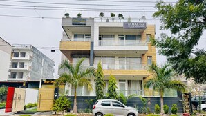 A multi-story hotel with balconies, a car parked in front, and a signboard listing amenities like a rooftop cafe and events. - the royal oak sec 40 hotel gurgaon (Gurugram)